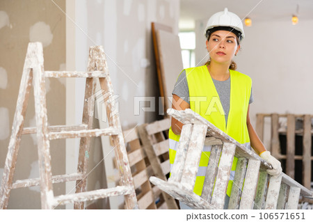 Portrait of woman in protective yellow vest and hard hat in room being renovated 106571651