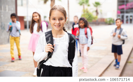 Positive schoolgirl standing near school, children on background Positive schoolgirl standing near school, children on background 106571714