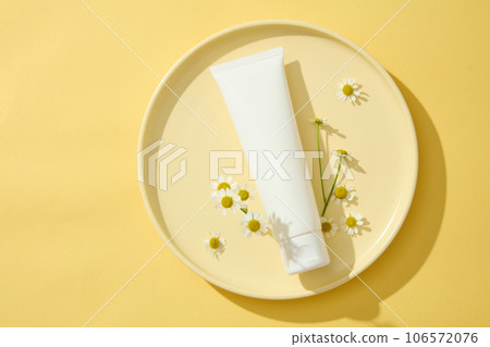 Yellow dish featured an empty label cosmetic tube with few Chamomile flowers. Copy space. Blemishes and redness can be lightened by Chamomilla (Matricaria chamomilla) 106572076