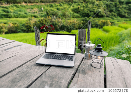 Laptop computer blank screen on a wooden terrace in the background of rice fields Laptop computer blank screen on a wooden terrace in the background of rice fields 106572578