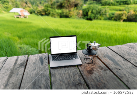 Laptop computer blank screen on a wooden terrace in the background of rice fields Laptop computer blank screen on a wooden terrace in the background of rice fields 106572582
