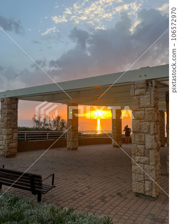 View of a beautiful sunset and a stone canopy gazebo on the seashore in Netanya 106572970