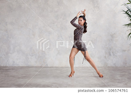 Woman dances flamenco. Female dancer stands in beautiful pose, dressed leopard dress against grey wall in studio Woman dances flamenco. Female dancer stands in beautiful pose, dressed leopard dress against grey wall in studio 106574761