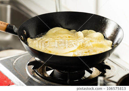 Potato slices being fried in a frying pan. 106575813