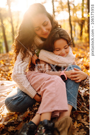 Stylish young Mother and daughter walking in the autumn forest at sunset. Family on a walk. 106575958