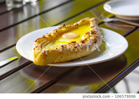 Adjara-style khachapuri, baked dough with egg, cheese and two pieces of butter on a white plate in a cafe. 106578006