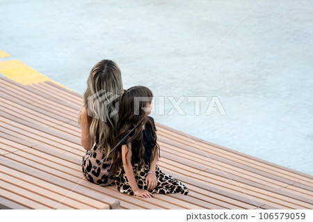 Back view long-haired mother and daughter sitting on bench Back view long-haired mother and daughter sitting on bench 106579059