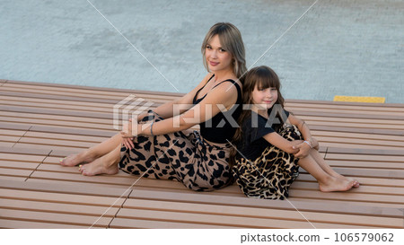 Long-haired mother and daughter sitting on bench back to back Long-haired mother and daughter sitting on bench back to back 106579062
