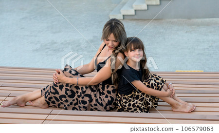 Long-haired mother and daughter sitting on bench back to back Long-haired mother and daughter sitting on bench back to back 106579063