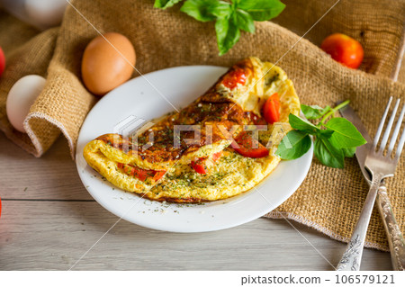 Stuffed omelette with tomatoes on a light wooden background. 106579121