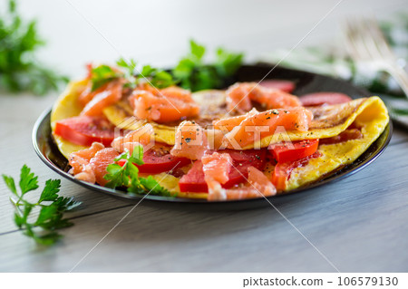 Fried omelette with tomatoes, vegetables and pieces of lightly salted red fish. 106579130