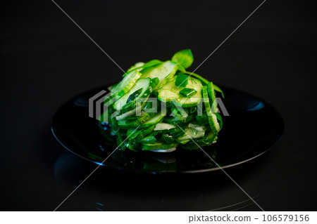 salad of fresh cucumbers with herbs and onions in a plate on a black background. salad of fresh cucumbers with herbs and onions in a plate on a black background. 106579156