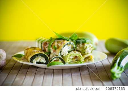 cooked zucchini rolls with cheese filling inside, in a plate 106579163