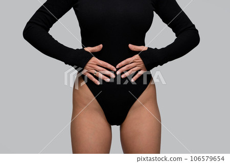 Close-up slender woman in black bodysuit holds hands on stomach Close-up slender woman in black bodysuit holds hands on stomach 106579654