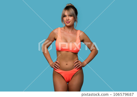 Slim woman posing wearing orange swimsuit on blue background 106579687