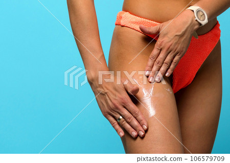 Woman in swimsuit applying moisturizing sunscreen cream to hip 106579709