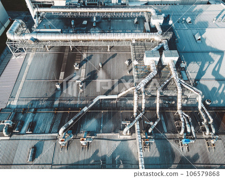 Directly above a roof top of an industrial building with ventilation pipes going across the roof Directly above a roof top of an industrial building with ventilation pipes going across the roof 106579868