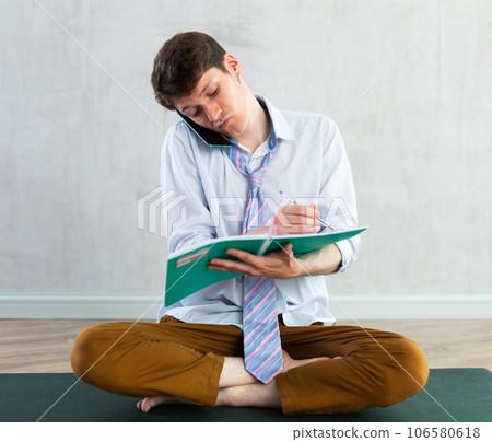 Young guy making notes while talking on phone 106580618