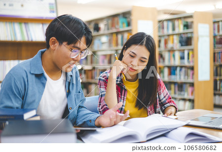 Students are consulting each other working on laptops and searching for books to study, make reports, find useful information in university room. Concept of reading, learning and intelligence. 106580682