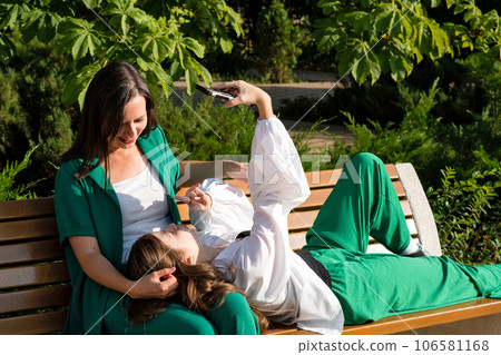 Mom and teenage daughter on park bench looking at mobile 106581168