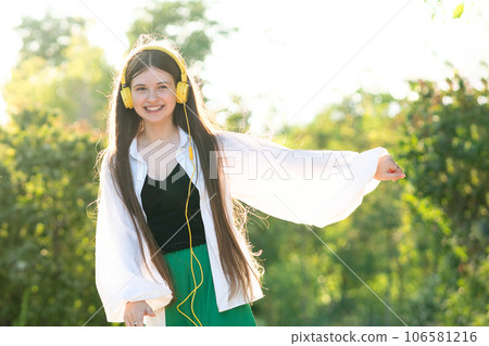 Teenage girl listening to music and dancing with headphones outdoors 106581216