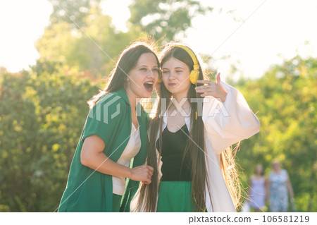 Mom and teen girl listening to music in headphones outdoors 106581219