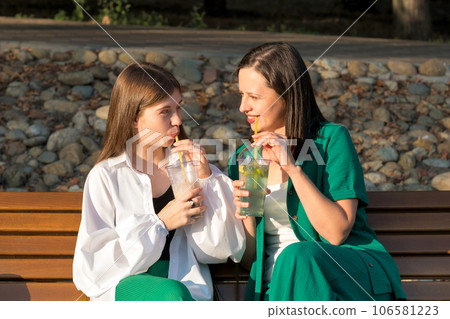 Mom and teenage daughter drink soft drinks on walk 106581223