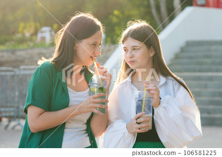 Mom and teenage daughter drink soft drinks on walk 106581225