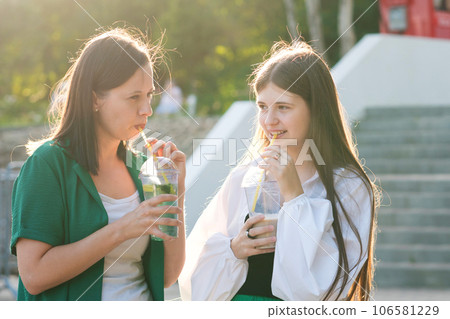 Mom and teenage daughter drink soft drinks on walk 106581229
