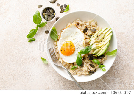 Savory oatmeal with fried sunny side up egg, avocado and pumpkin seeds for healthy breakfast Savory oatmeal with fried sunny side up egg, avocado and pumpkin seeds for healthy breakfast 106581307