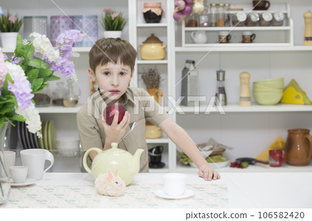 Boy in the kitchen with a red apple.A child with a ripe apple. Healthy breakfast Boy in the kitchen with a red apple.A child with a ripe apple. Healthy breakfast 106582420