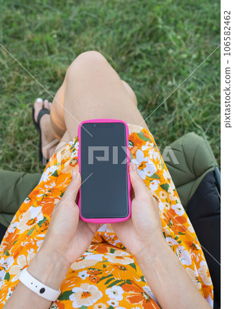 A girl sits on a chair in nature and holds a smartphone mockup with a blank screen. The concept of communication via the Internet. A girl sits on a chair in nature and holds a smartphone mockup with a blank screen. The concept of communication via the Internet. 106582462