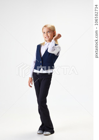 Full-length portrait of beautiful school girl, child in stylish uniform standing with smile against white studio background 106582734