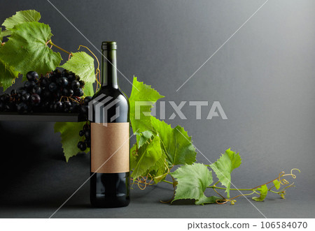 Bottle of red wine with blue grapes and vine branches. 106584070