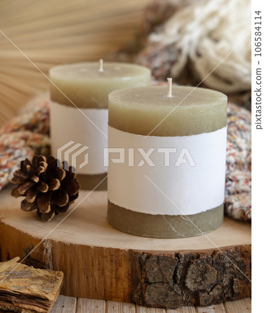 Candles with blank label near pine cones and cream sweater, Close up, copy space, mock up 106584114