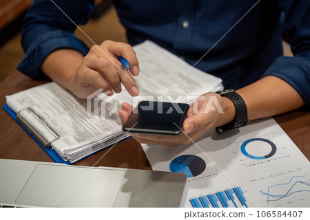 Report charts and graphs marketing financial business analysis and data insights. Hand man holding mobile smartphone on desk. Report charts and graphs marketing financial business analysis and data insights. Hand man holding mobile smartphone on desk. 106584407