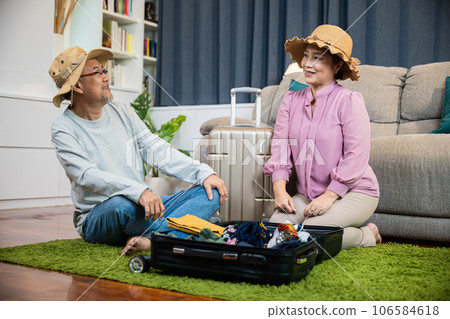 Asian romantic retired couple packing clothes travel bag suitcase together on floor at home interior living room, couple old senior married retired prepare luggage suitcase arranging for travel Asian romantic retired couple packing clothes travel bag suitcase together on floor at home interior living room, couple old senior married retired prepare luggage suitcase arranging for travel 106584618
