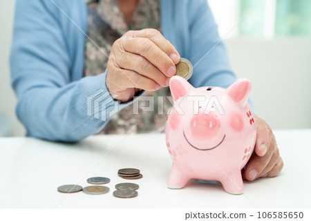 Asian elderly woman putting coin into pink piggy bank for saving money and insurance, poverty, financial problem in retirement. Asian elderly woman putting coin into pink piggy bank for saving money and insurance, poverty, financial problem in retirement. 106585650