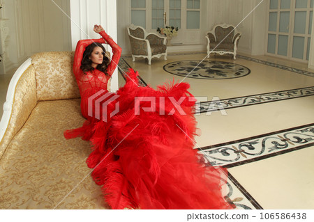 Beautiful woman in glamorous red dress on sofa in luxurious interior with classic style tiles Beautiful woman in glamorous red dress on sofa in luxurious interior with classic style tiles 106586438