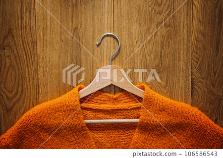 Autumn fall minimalist wardrobe with orange warm knitted sweater on wooden clothes hanger. Autumn capsule, warm fashion trends and stylish warm background, knitwear, copy space. 106586543