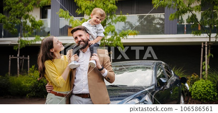 Happy family standing in front their electric car and charging it on the street. 106586561