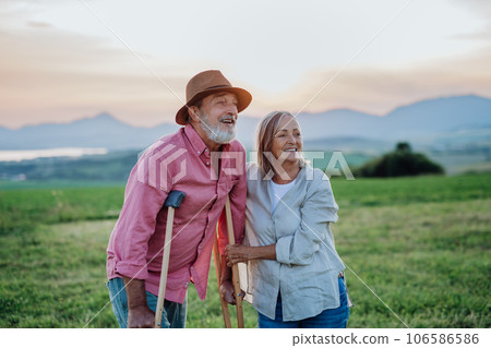 Senior man with broken leg and crutches standing in the the middle of meadow. 106586586