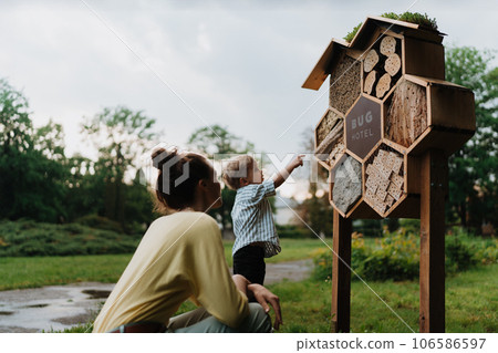 Mom showing her playful son an insect hotel in public park. 106586597