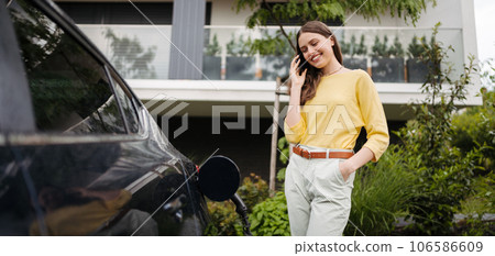 Close up of beautiful woman calling while charging her electric car on the street. 106586609