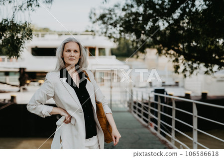 Portrait of beautiful female manager in middle age with gray hair walking through the city. 106586618