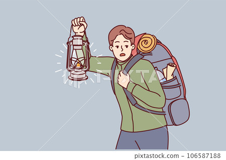 Man is engaged in hiking and carries large backpack on back, holding kerosene lantern to light way in dark 106587188