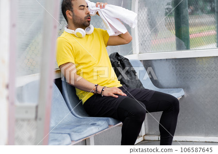 tired man portrait wiping sweat face with towel sitting in small arbor stadium after sport training athlete resting after hard workout on outdoor athletic arena tired man portrait wiping sweat face with towel sitting in small arbor stadium after sport training athlete resting after hard workout on outdoor athletic arena 106587645