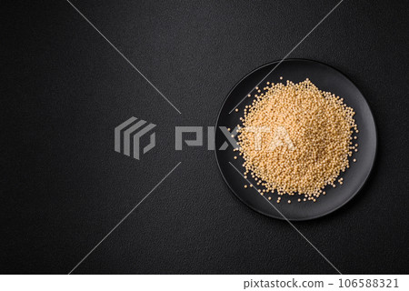 Raw ptitim pasta in a ceramic bowl on a dark concrete background 106588321