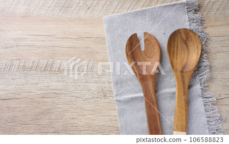 Two wooden spoons on a gray textile kitchen towel on a wooden background, top view Two wooden spoons on a gray textile kitchen towel on a wooden background, top view 106588823