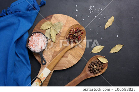 Peppercorns and salt in a wooden spoon on a black table, top view 106588825